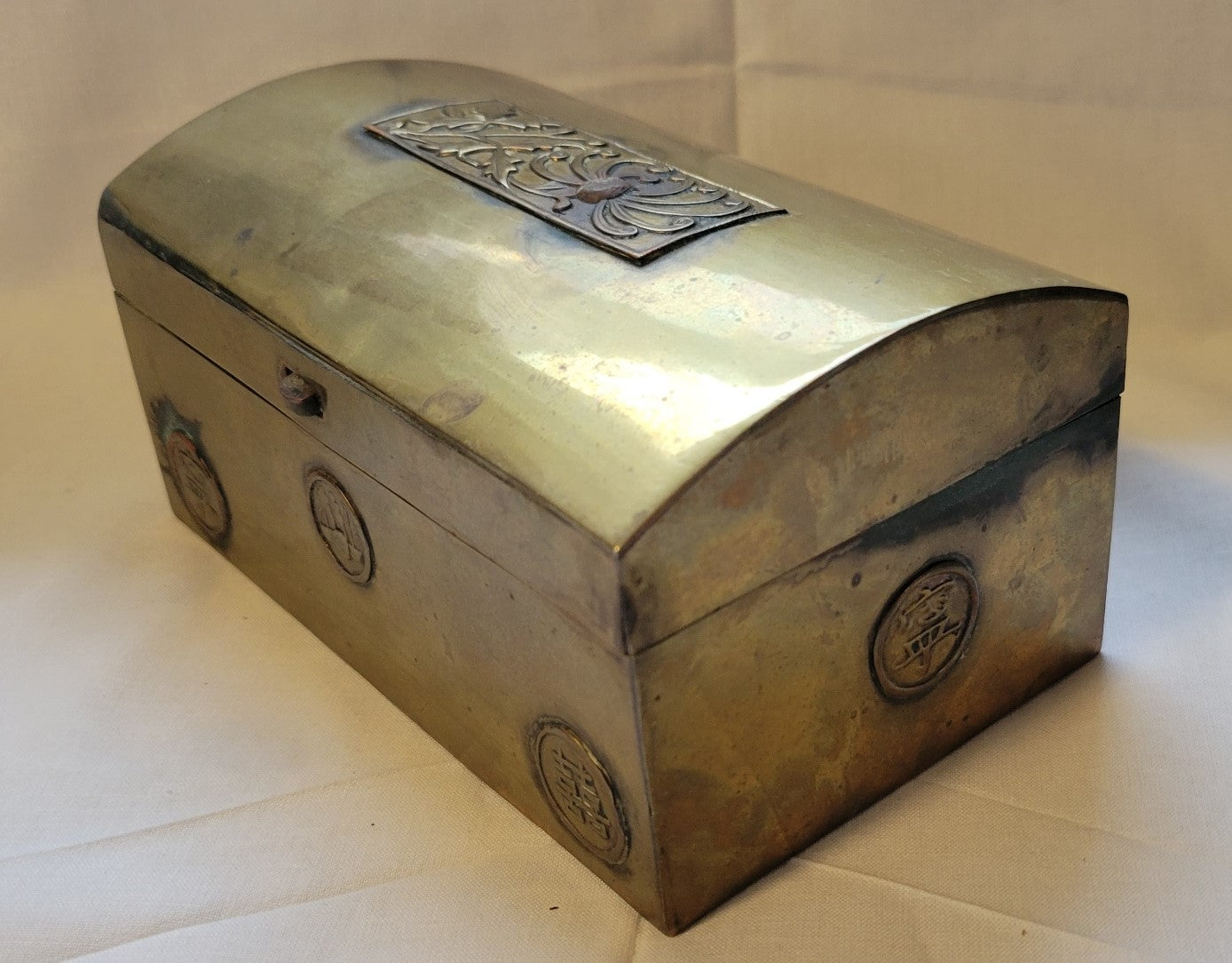 Antique brass box curio made in China, with a domed lid. The interior bottom has wood inserts on three side (one side is missing). The exterior has welded medallions with Chinese characters and designs. View of opposite corner.